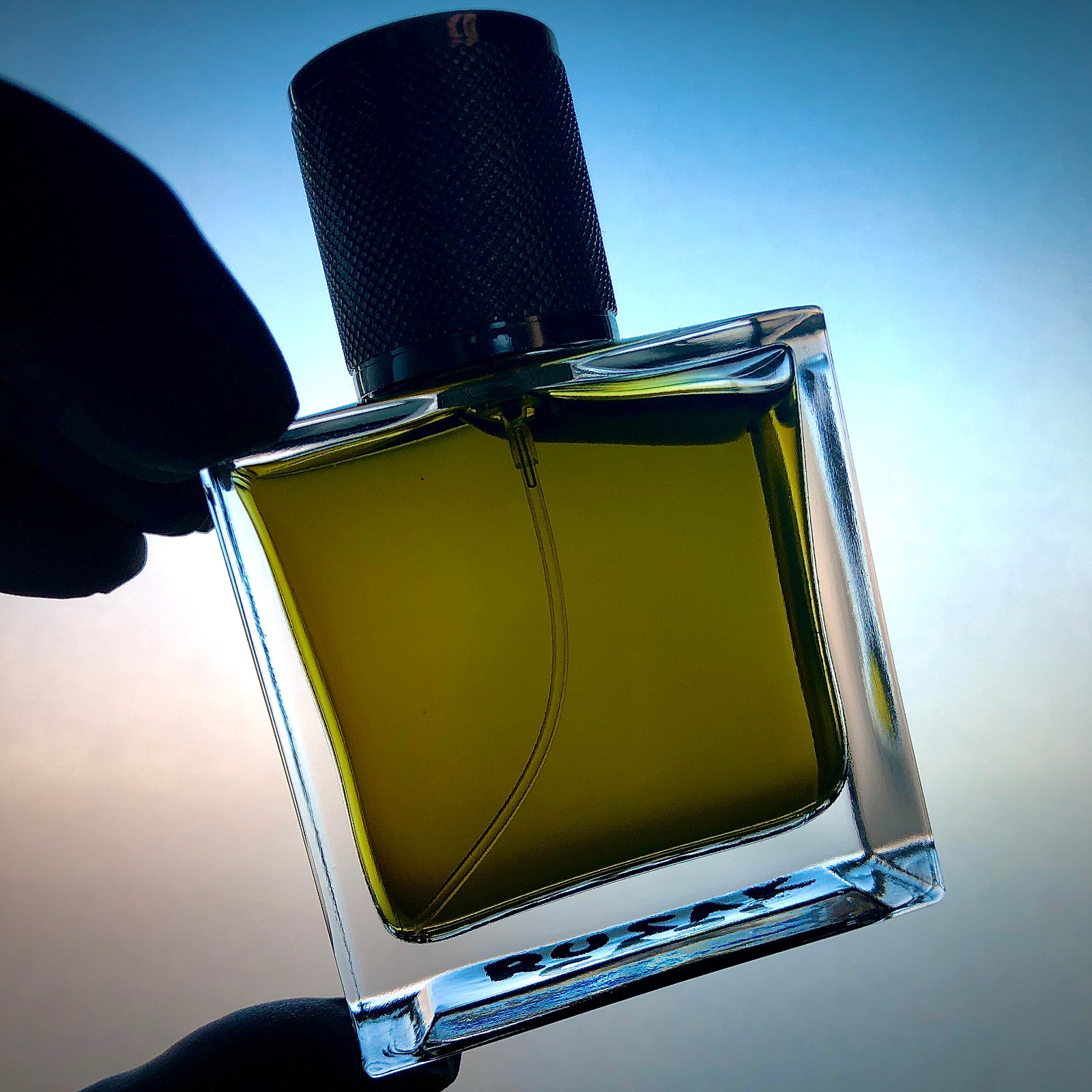 Perfume bottle with dark-green juice, handheld against a backlit screen.