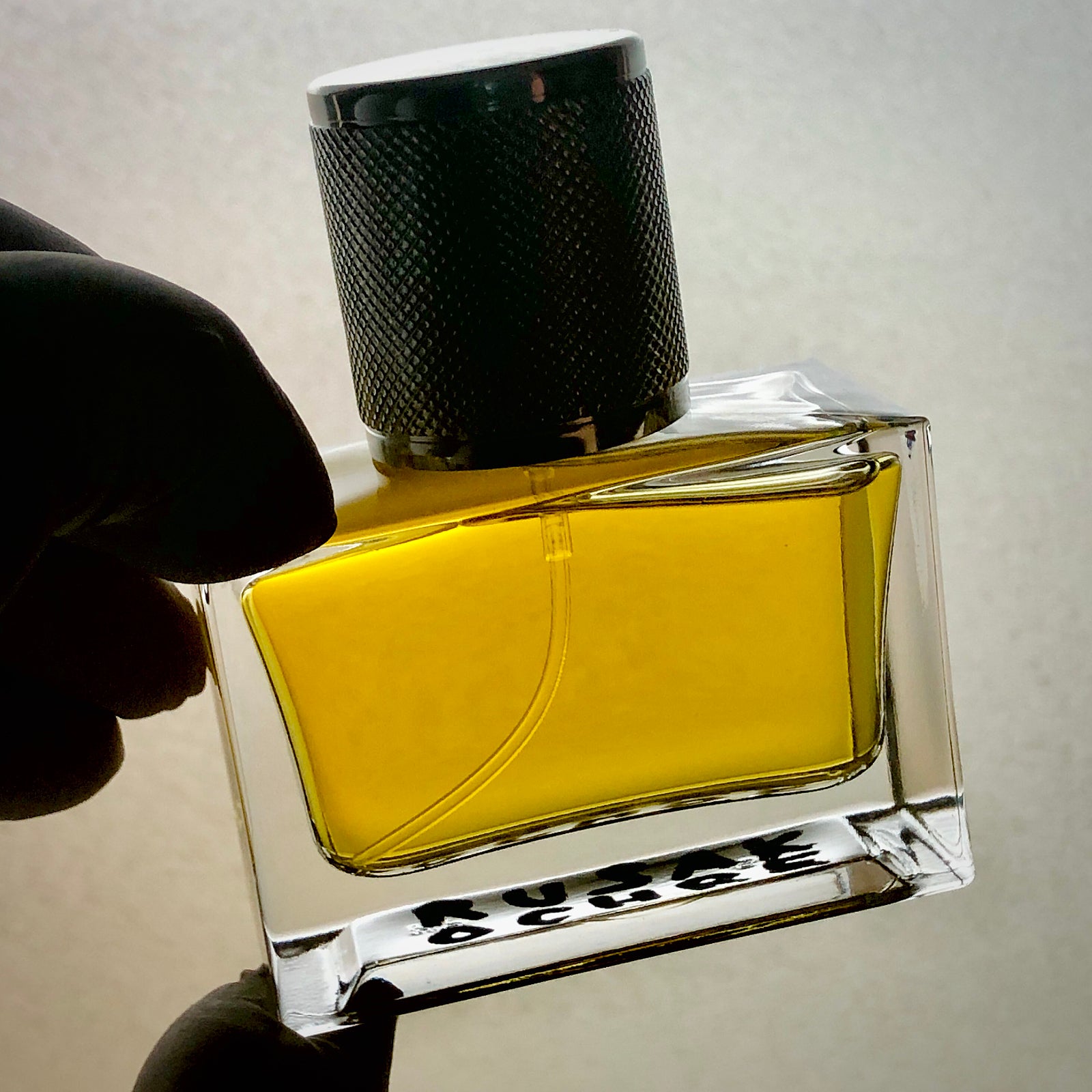 Perfume bottle with ochre-colored juice, held in a hand, backlit.